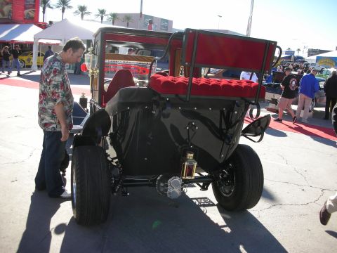1998 Ford Crown Victoria - A man examines the rear of a black antique car with red tufted seats at an outdoor event.