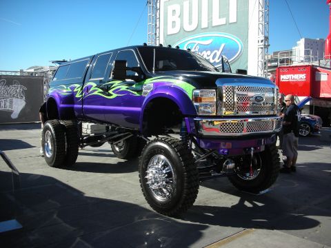 1998 Ford Crown Victoria - A heavily modified Ford Super Duty truck is displayed outdoors with a large Ford banner in the background.