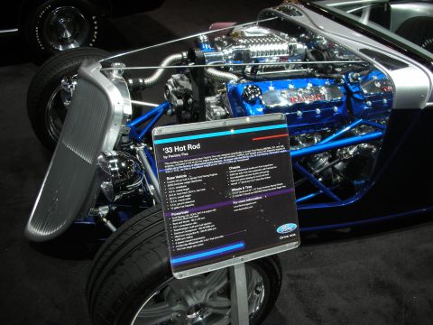 1998 Ford Crown Victoria - A hot rod with a prominent supercharged engine is displayed with an informational sign.