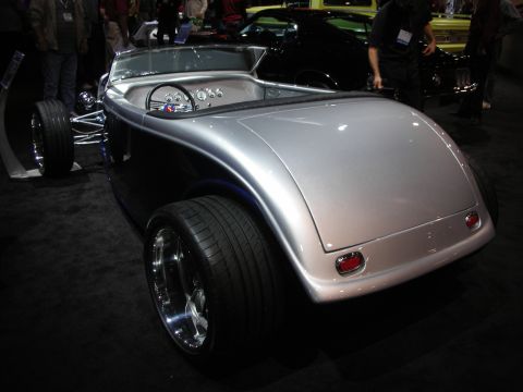 1998 Ford Crown Victoria - A silver hot rod convertible is displayed indoors with other vehicles in the background.