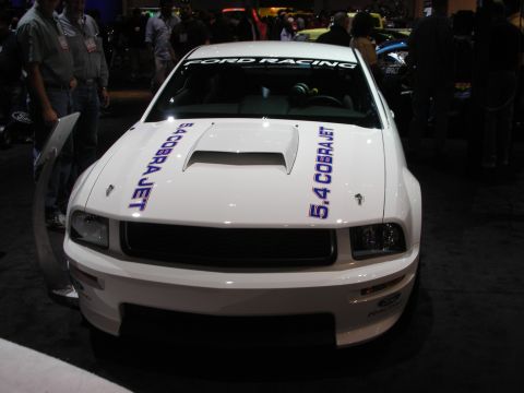 1998 Ford Crown Victoria - A white Ford Mustang with racing decals is displayed indoors.