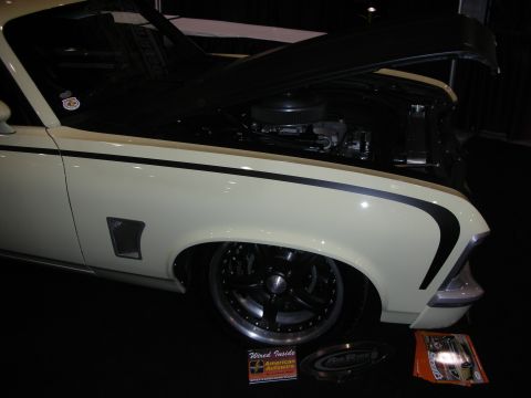 1998 Ford Crown Victoria - A cream-colored car with black racing stripes and custom wheels is displayed with its hood open, revealing the engine bay.