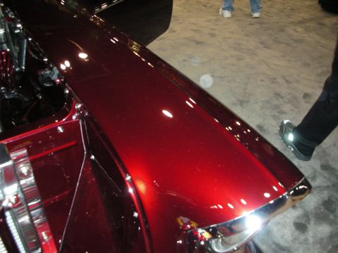 1998 Ford Crown Victoria - Close-up of a shiny red car fender with chrome accents, showing part of the engine bay.