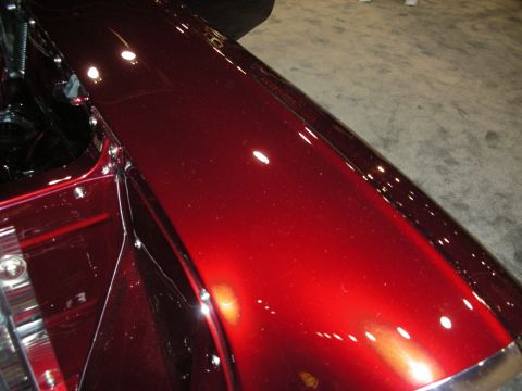 1998 Ford Crown Victoria - Close-up view of a shiny red metallic fender, likely from a custom or classic vehicle, showing rivets and chrome accents.
