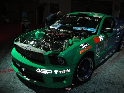 1998 Ford Crown Victoria - A green Ford Mustang, likely from the mid-2000s, is displayed with its hood open, revealing the engine and various racing decals.