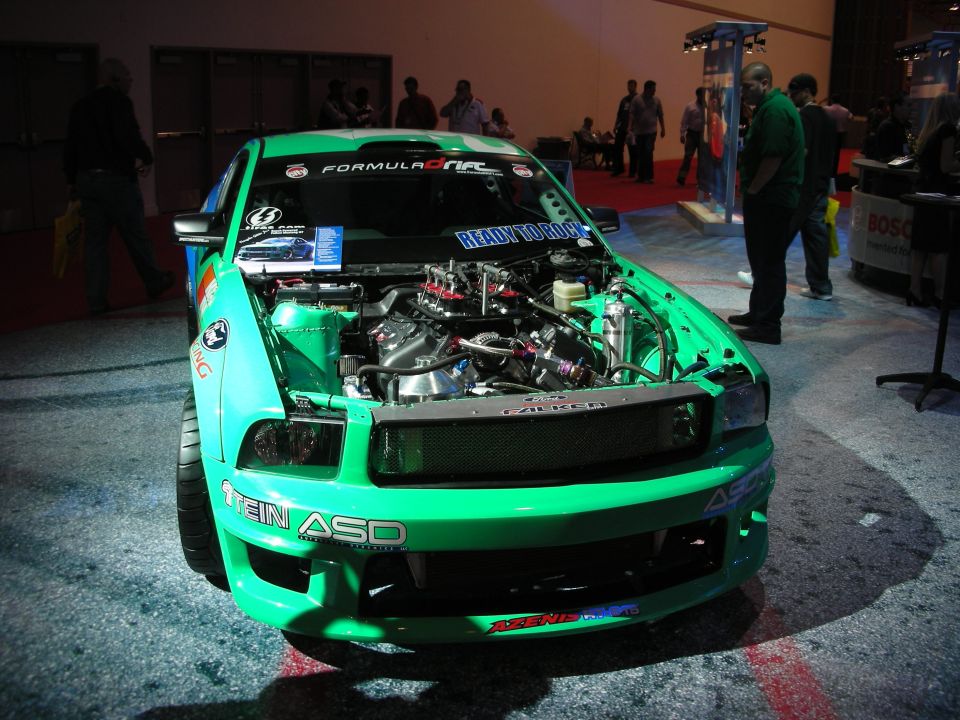 Green custom Ford Mustang, hood open showing engine. "STEIN ASD" sticker on bumper
