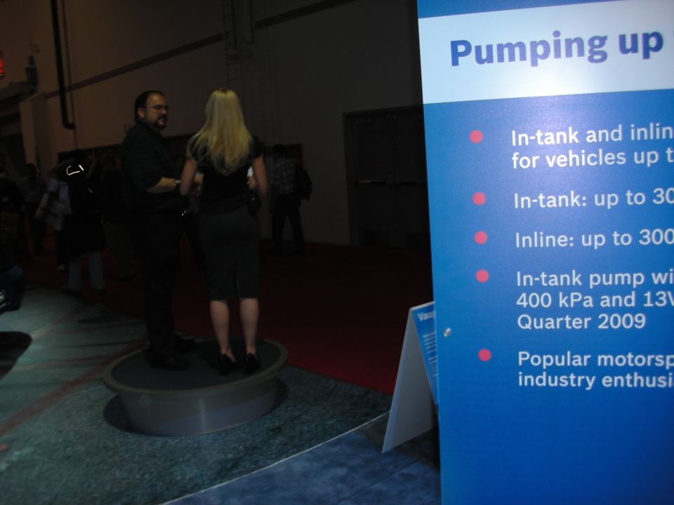 Two people stand near a blue display board with text about fuel pumps