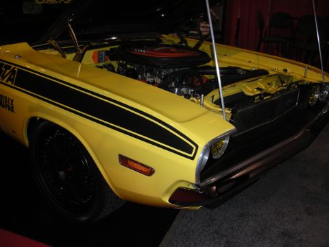 1998 Ford Crown Victoria - A yellow 1970 Dodge Challenger R/T is displayed with its hood open, revealing the engine and black racing stripes on its side.