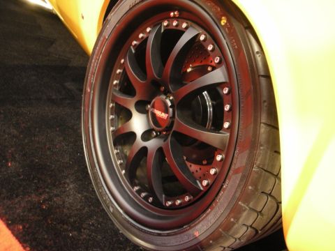 1998 Ford Crown Victoria - A close-up shot focuses on a custom black wheel with a red center cap, mounted on a yellow vehicle.