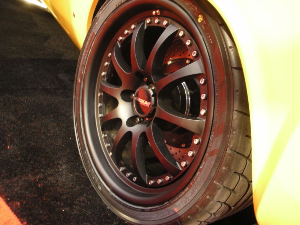 Close-up of a black multi-spoke aftermarket wheel with a red 'Forgeline' center cap on a yellow car