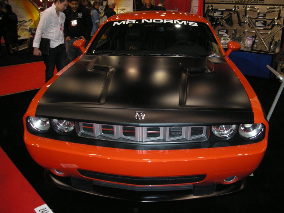 Orange Dodge Challenger with a black hood and a "MR. NORM'S" windshield banner, viewed from the front