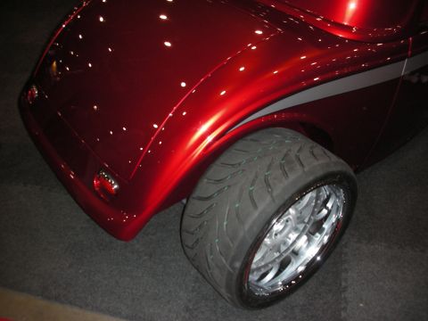 1998 Ford Crown Victoria - A custom red hot rod car is shown from the rear quarter panel, highlighting its wide tire and custom wheels.