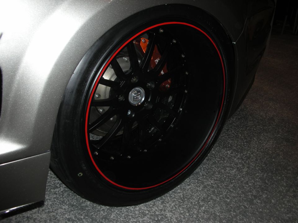 Close-up of a custom black wheel with a red pinstripe, showing an orange brake caliper behind the spokes