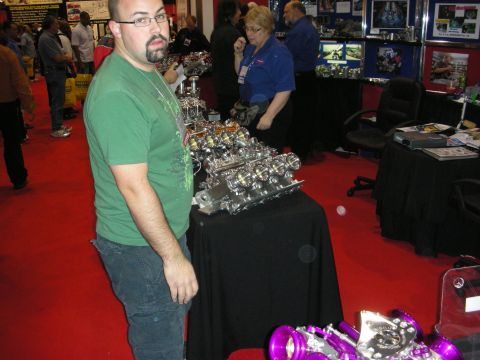 1998 Ford Crown Victoria - A man in a green t-shirt stands near a display of automotive parts at a convention.