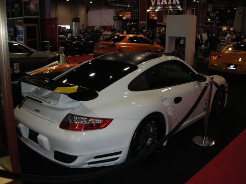 1998 Ford Crown Victoria - A white Porsche 911 is displayed indoors, with other vehicles in the background.