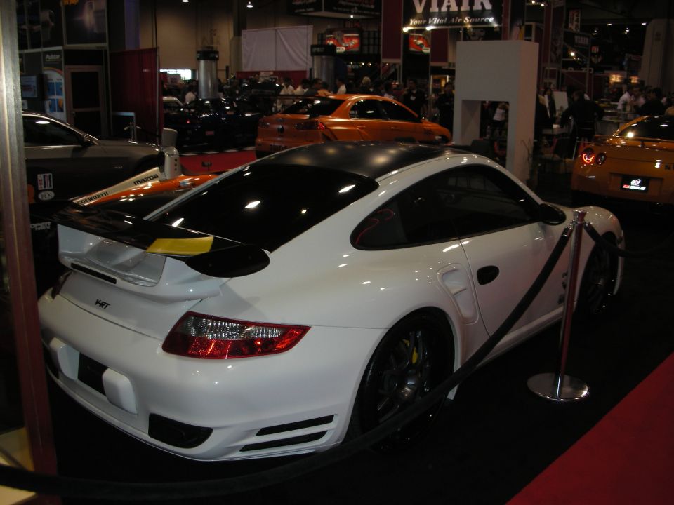 White Porsche 911 with black roof and spoiler, parked indoors with other cars visible