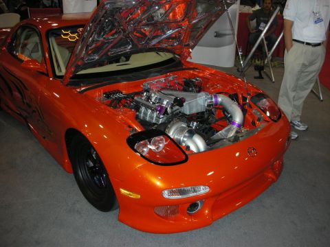 1998 Ford Crown Victoria - A highly modified orange sports car is displayed with its hood open, revealing a custom engine setup.