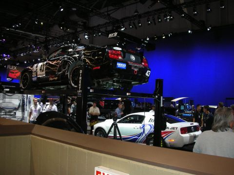 1998 Ford Crown Victoria - Two custom race cars are displayed at an event, one elevated on a lift and the other positioned beneath it.
