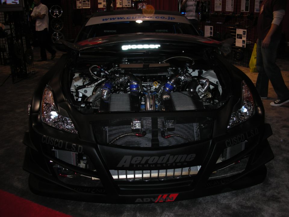 Modified car engine bay with twin turbos and intercoolers visible. "CUSCO L.S.D." and "Aerodyne Industries" text on the front