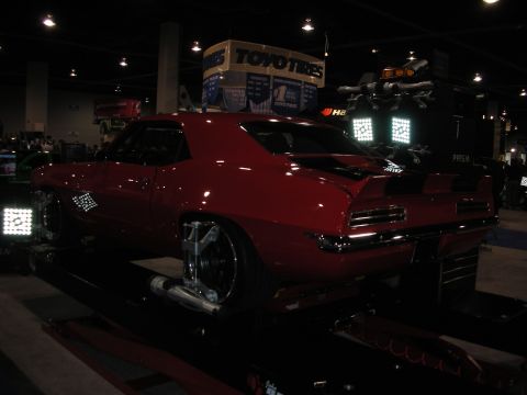 1998 Ford Crown Victoria - A red 1969 Chevrolet Camaro is positioned on an alignment rack in a dimly lit exhibition hall.
