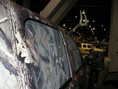 1998 Ford Crown Victoria - A truck with a camouflage wrap and deer antlers mounted on the roof is displayed indoors, with other vehicles visible in the background.