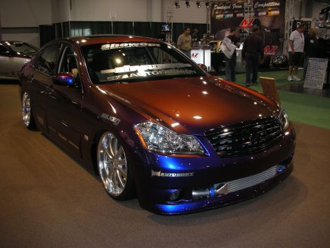 1998 Ford Crown Victoria - A modified sedan with a unique paint job and custom wheels is displayed indoors, with other vehicles and people in the background.
