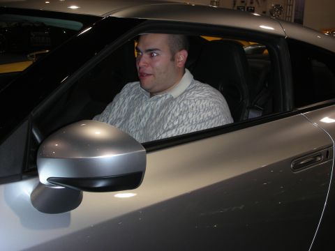 1998 Ford Crown Victoria - A man is seated inside a silver car, looking towards the side.