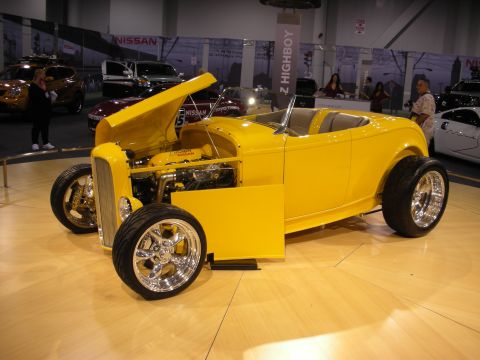1998 Ford Crown Victoria - A bright yellow custom hot rod is displayed indoors with its hood open, revealing the engine and other components.