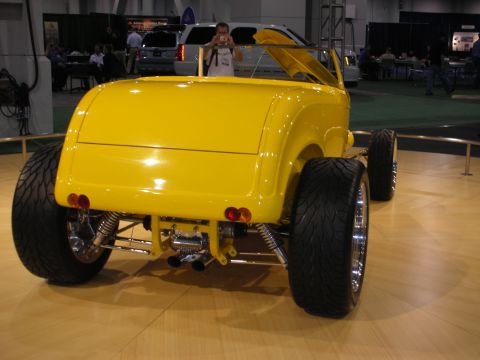 1998 Ford Crown Victoria - A bright yellow hot rod is displayed indoors, its custom rear suspension and wide tires.
