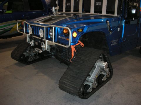 1998 Ford Crown Victoria - A blue tracked vehicle with a brush guard and orange straps is displayed indoors, with another blue vehicle visible behind it.