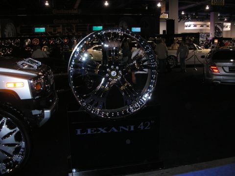 1998 Ford Crown Victoria - A large, highly polished chrome wheel is displayed at an automotive event, with other vehicles in the background.