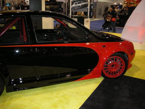 1998 Ford Crown Victoria - A modified hatchback with a two-tone black and red paint scheme and red racing wheels is displayed indoors.