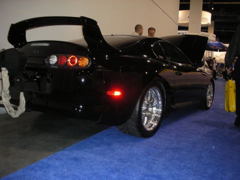 1998 Ford Crown Victoria - Black sports car with a prominent rear spoiler and custom wheels is displayed indoors.