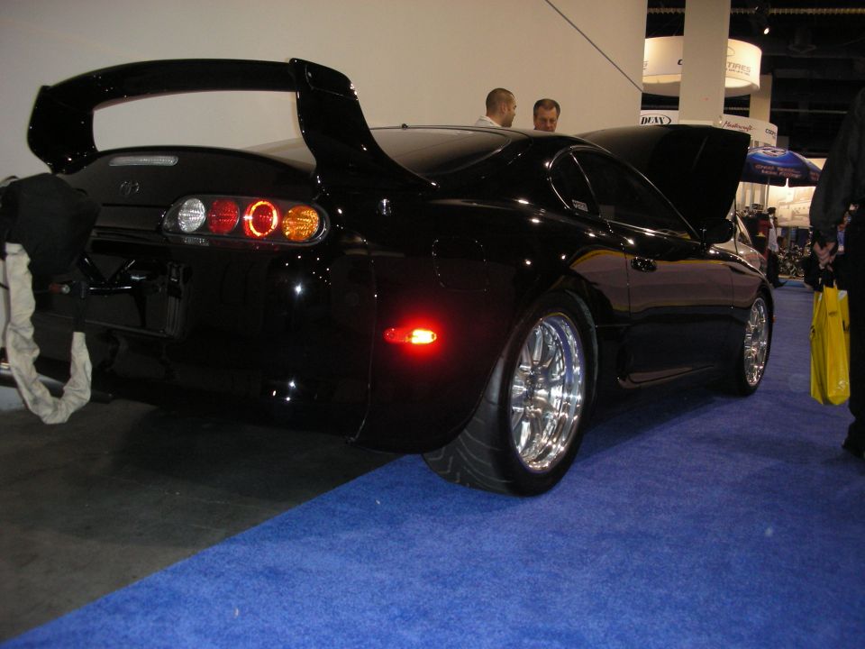 Black sports car with large rear spoiler and chrome wheels. Hood is open
