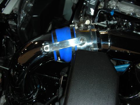 1998 Ford Crown Victoria - Close-up view of engine components, including a shiny intake pipe and a blue rubber connector.