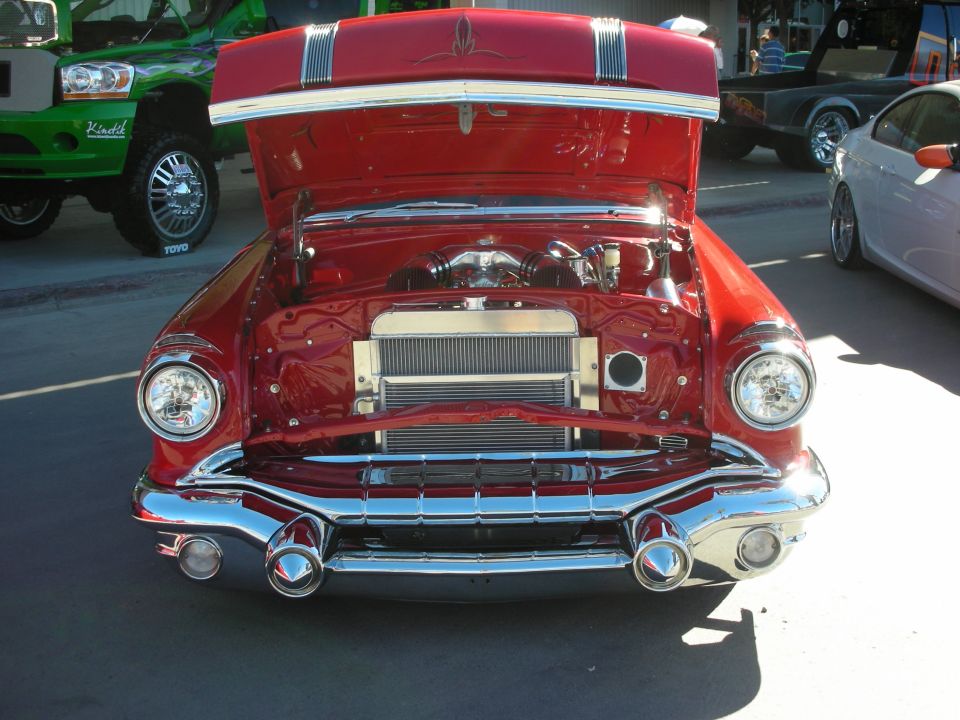 Red classic car front view, hood open showing engine and radiator. Chrome grille and bumper