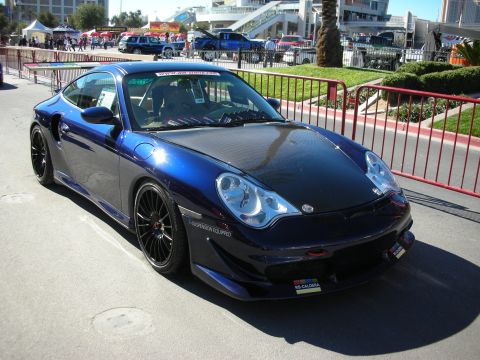 1998 Ford Crown Victoria - A blue Porsche 911 with a carbon fiber hood and racing decals is parked at an outdoor event.