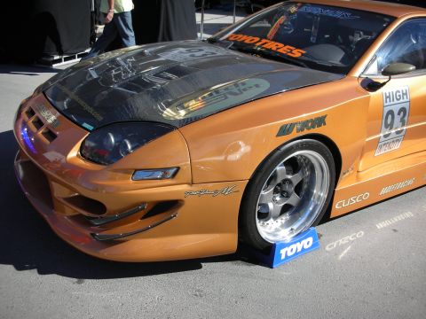 1998 Ford Crown Victoria - A modified orange sports car is displayed with racing decals and custom wheels.
