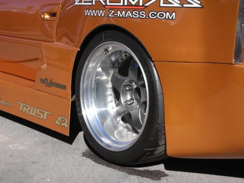 1998 Ford Crown Victoria - Close-up of a custom orange car's rear wheel, a chrome rim and "TRUST" decal on the body kit.