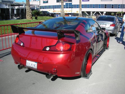 1998 Ford Crown Victoria - A modified red Infiniti coupe is parked outdoors, its aggressive rear spoiler and custom wheels.