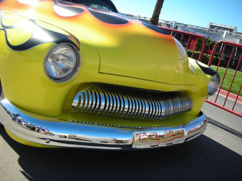 1998 Ford Crown Victoria - A bright yellow classic car with flame graphics on the hood and a distinctive chrome grille is parked outdoors.