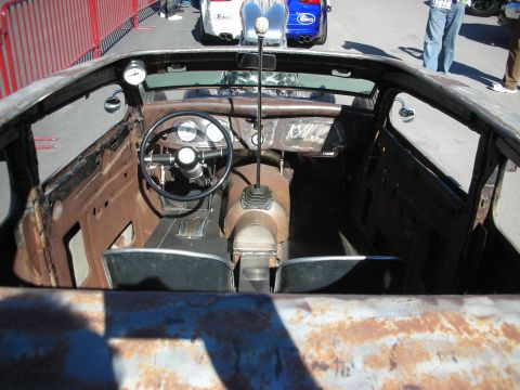 1998 Ford Crown Victoria - The interior of a heavily modified hot rod shows exposed metal and custom gauges, with other vehicles in the background.