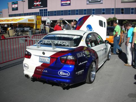 1998 Ford Crown Victoria - A customized BMW sedan with a distinctive red, white, and blue livery and a prominent rear spoiler is displayed at an event.