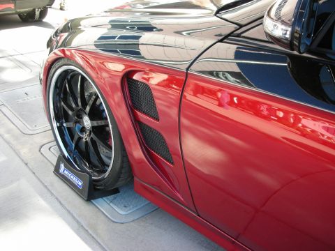 1998 Ford Crown Victoria - A close-up view of a red sports car's fender and wheel, custom body modifications and large black rims.