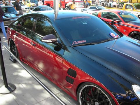 1998 Ford Crown Victoria - A custom two-tone car with red and black paint is displayed at an outdoor event, with other vehicles visible in the background.