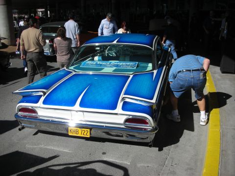 1998 Ford Crown Victoria - A man inspects a vintage car with a custom blue paint job and distinctive tail fins.