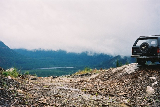 Dark Ford SUV with rear-mounted spare tire parked on a mountain overlook with cloudy valley below