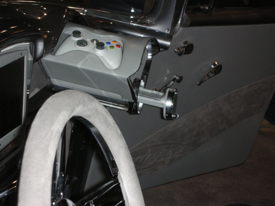 Car interior with a white Xbox controller mounted on the dash and a screen to the left of the steering wheel
