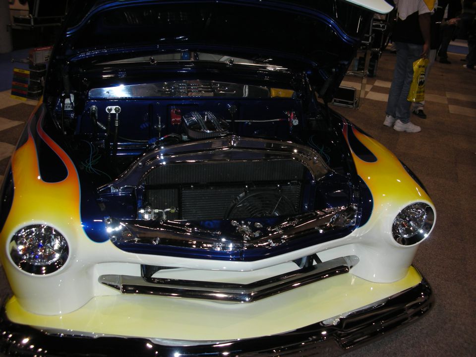 Front view of a blue and white hot rod with yellow and orange flames, chrome grille, and exposed engine
