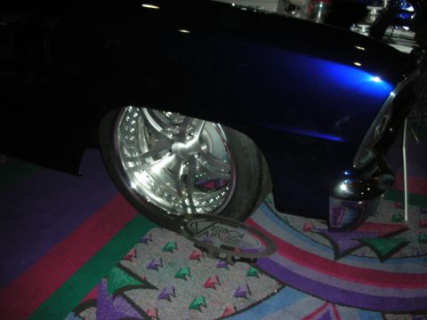 1998 Ford Crown Victoria - A close-up of a customized car's front fender and wheel, with a hubcap displaying 'VINTAGE AIR' resting on the carpet.
